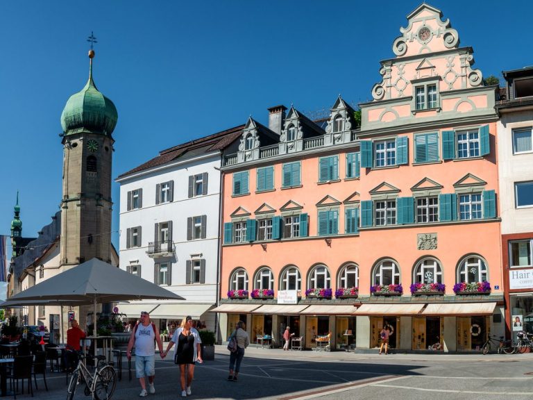 Bellavista-Brand Bregenz Innenstadt Stadtplatz Bregenz mit historischen Gebäuden, einem Uhrturm und Gästen bei strahlendem Wetter.